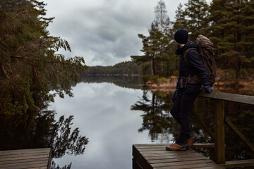A caucasian man hiker standing on a wooden jetty over looking a  lake in the forest watching reflections in the water.
