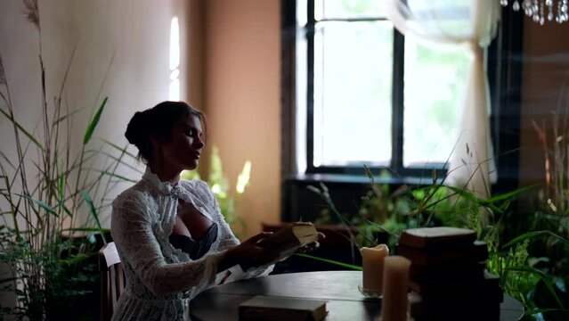 beautiful busty woman in vintage dress is reading novels in library of old house