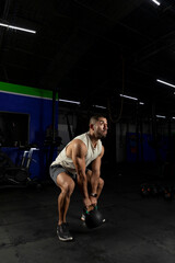 Fototapeta na wymiar Vertical shot of a Latino man exercising in a gym using a kettlebell