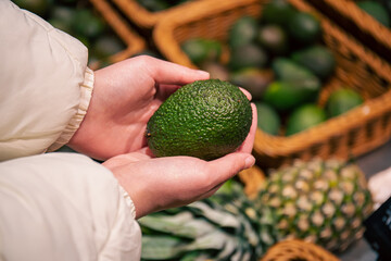 A woman chooses an avocado in a grocery store.