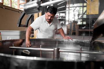 An Hispanic man is cleaning the coffee roaster machine cooling tray