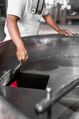 An Hispanic man is cleaning the coffee roaster machine cooling tray