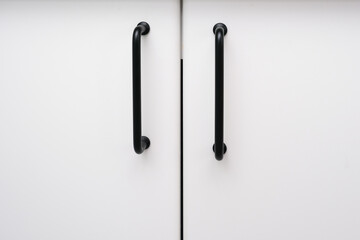 White kitchen cabinets with metal black pulls or knobs, handles on the doors close up background