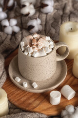 Fototapeta na wymiar Cozy home still life: a cup of hot chocolate or cocoa with marshmallows on a wooden board, a wool sweater, candles and a sprig of cotton.