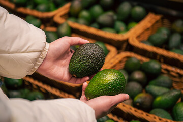 A woman chooses an avocado in a grocery store.