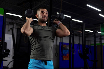 Mexican man in sportswear exercising in a gym using two dumbbells