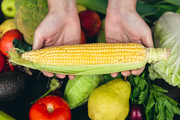 Close-up, corn in female hands and other vegetables on the kitchen table.