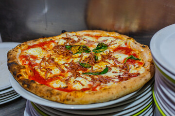 Pizza tradizionale napoletana con sugo di pomodoro, salame piccante, basilico, mozzarella e basilico pronta per essere servita in una pizzeria napoletana