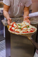 Pizzaiolo napoletano mentre stende sulla pala una pizza margherita napoletana con sugo di pomodoro, mozzarella e basilico pronta per essere infornata