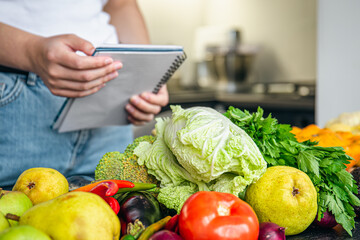 Woman with notepad and vegetables on the kitchen table preparing a recipe.