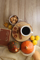 Cup of tea or coffee, seasonal spices, bowl of cookies, blanket, pumpkins, colorful leaves, books and tangerines on wooden table. Cozy hygge at home. Top view.