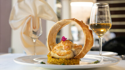 beautifully served fish in cream sauce with rice. a glass of white wine and restaurant background