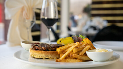 Tasty burger with beef, tomatoes, onion, pickles, and french fries. Restaurant background. 