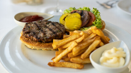 Tasty burger with beef, tomatoes, onion, pickles, and french fries. Restaurant background. 