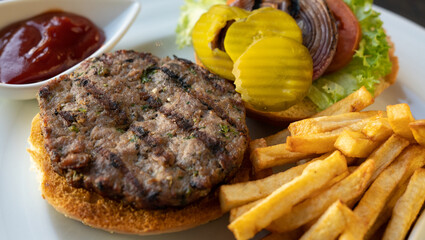 Tasty burger with beef, tomatoes, onion, pickles, and french fries. Restaurant background. 