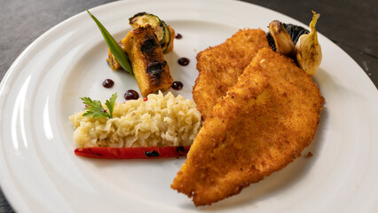 breaded fried chicken breast with vegetables, mashed potatoes and green leaves. black background