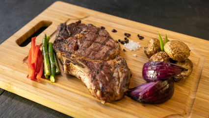 steak with vegetables, baked potatoes, onions and asparagus on a wooden tray. black background