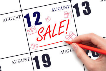Hand writing text SALE and drawing gift boxes on calendar date August 12. Shopping Reminder