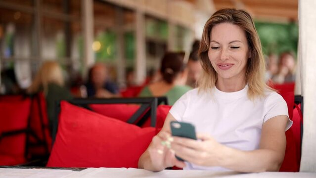 happy woman is using smartphone in cafe, viewing pictures, video and reading posts in social media