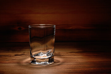 Empty shot glass against the background of the darkened wooden texture of the table