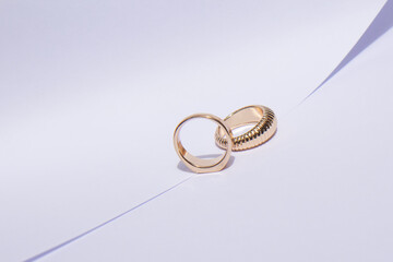 Two gold wedding rings on a white background with contrasting shadows