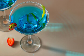 Glass with blue margarita cocktail garnished with lime zest and strawberries, selective focus