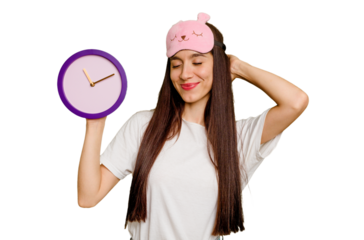 Young caucasian woman wearing pajama and holding a clock touching back of head, thinking and making a choice.