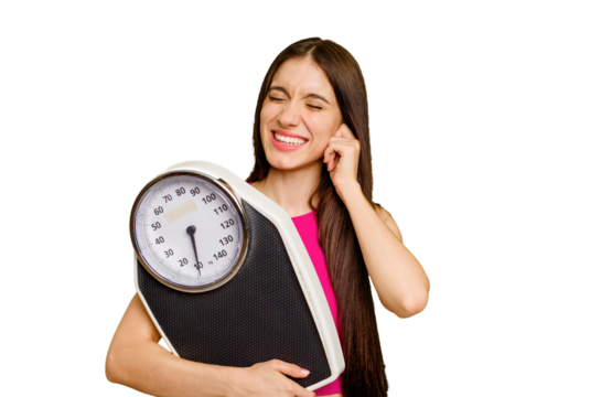 Young caucasian woman holding a scale isolated covering ears with hands.