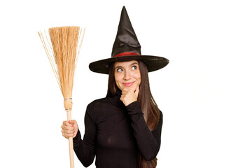 Young caucasian woman dressed as a witch holding a broom isolated looking sideways with doubtful and skeptical expression.
