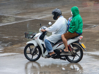 A couple in a raincoat is riding a motorbike on a wet road