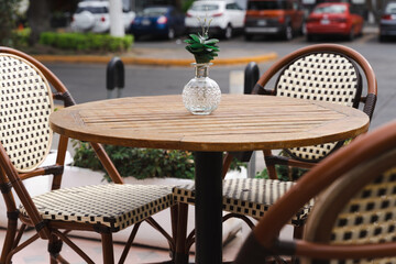 Glass flowerpot on wooden table and empty chairs at cafe terrace. Low season, outdoor decoration...