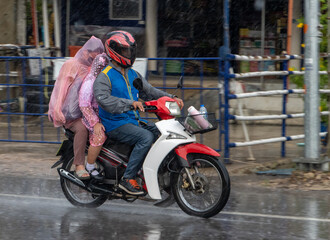 Obraz na płótnie Canvas A moto taxi driver with a woman and a girl in a raincoat ride down the street in heavy rain