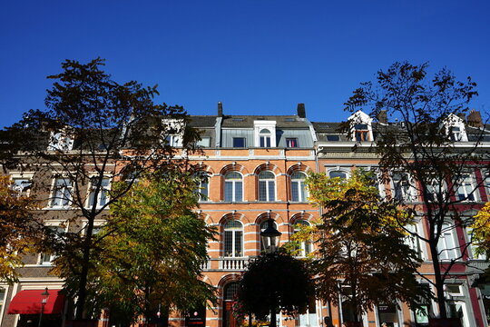 Altbauten mit sch&ouml;nen sanierten Fassaden und Dachwohnungen mit B&auml;umen in der Station Straat vor blauem Himmel im Sonnenschein in Maastricht an der Maas in der Provinz Limburg der Niederlande