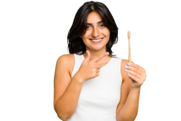 Young Indian woman holding a toothbrush isolated smiling and pointing aside, showing something at blank space.
