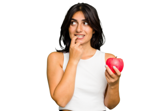 Young Indian woman holding an apple, healthy lifestyle, isolated relaxed thinking about something looking at a copy space.
