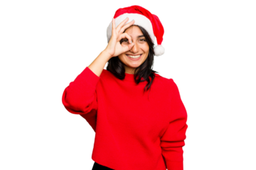 Young Indian woman celebrating Christmas wearing a santa hat isolated excited keeping ok gesture on eye.