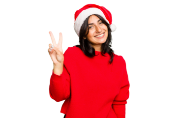 Young Indian woman celebrating Christmas wearing a santa hat isolated joyful and carefree showing a peace symbol with fingers.