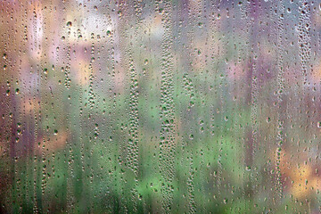 Motley colorful blur autumn background front view through rain droplets on window glass closeup