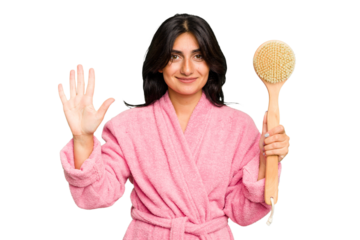 Young Indian woman in a bathrobe holding a back scratcher isolated smiling cheerful showing number five with fingers.