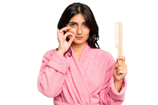 Young woman in a bathrobe holding an hair comb isolated with fingers on lips keeping a secret.