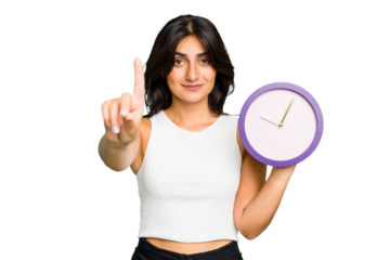 Young Indian woman holding a clock isolated showing number one with finger.