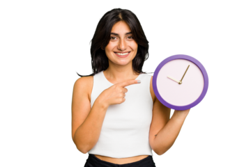 Young Indian woman holding a clock isolated smiling and pointing aside, showing something at blank space.