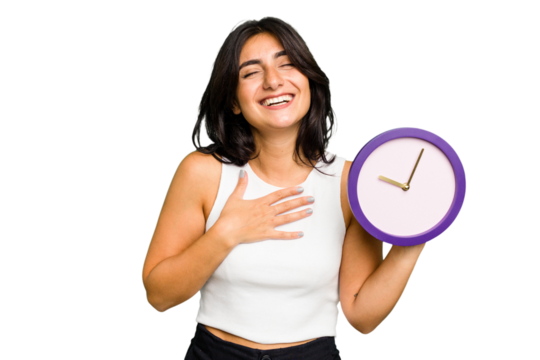 Young Indian woman holding a clock isolated laughs out loudly keeping hand on chest.
