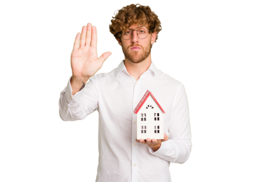 Business caucasian man holding toy house isolated on white background standing with outstretched hand showing stop sign, preventing you.