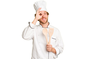 Young cook man isolated on white background excited keeping ok gesture on eye.