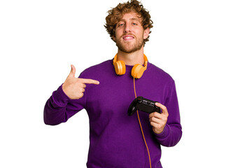 Young caucasian gamer man holding a game controller isolated on white background person pointing by hand to a shirt copy space, proud and confident - obrazy, fototapety, plakaty