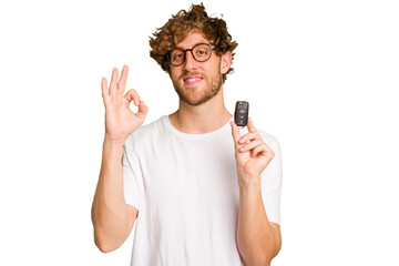 Young caucasian man holding car keys isolated on white background cheerful and confident showing ok...