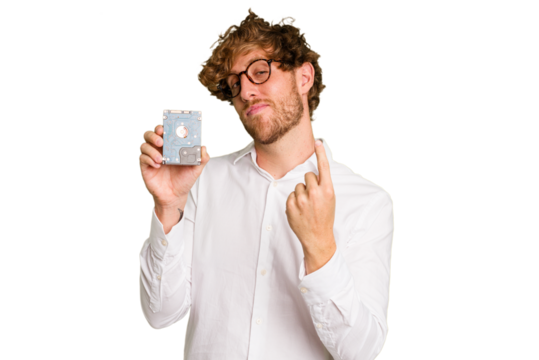 Young caucasian informatic man holding a hard drive isolated on white background pointing with finger at you as if inviting come closer.