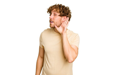 Young caucasian man isolated on green chroma background trying to listening a gossip.