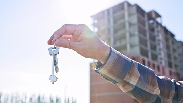 Keys to apartment, house in male hands against the backdrop of an apartment building under construction close-up. Buying an apartment, renting, renting a house, mortgage, loan